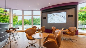 A modern meeting room with a large projection screen, comfortable seating, and large windows offering a view of the outdoors. - Designhotel Wienecke XI. Hannover (Hannover)