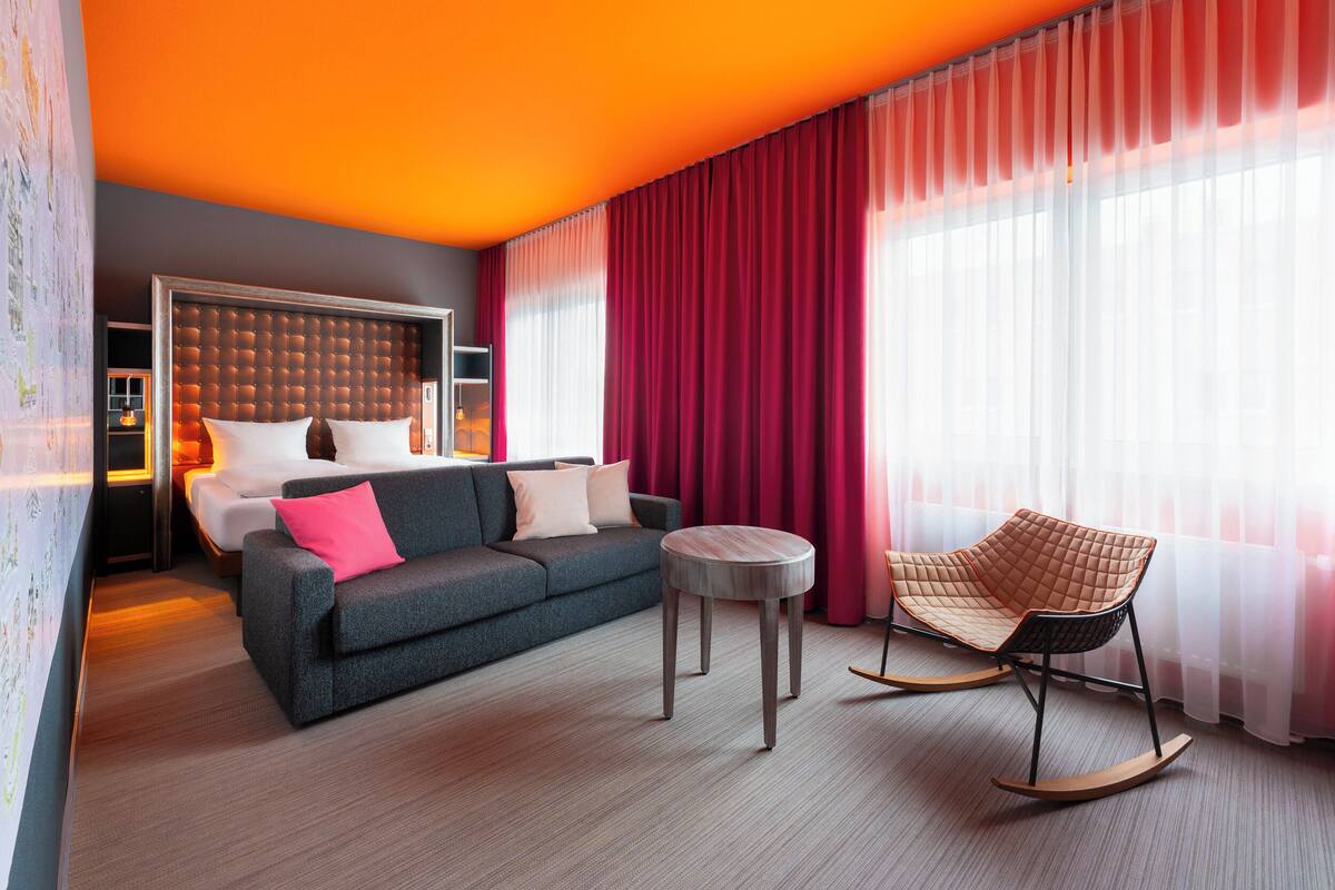 Een moderne hotelkamer met een groot bed, een grijze bank, een schommelstoel en een kleine tafel.