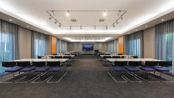 A conference room with multiple tables and chairs, a large screen, and a carpeted floor.