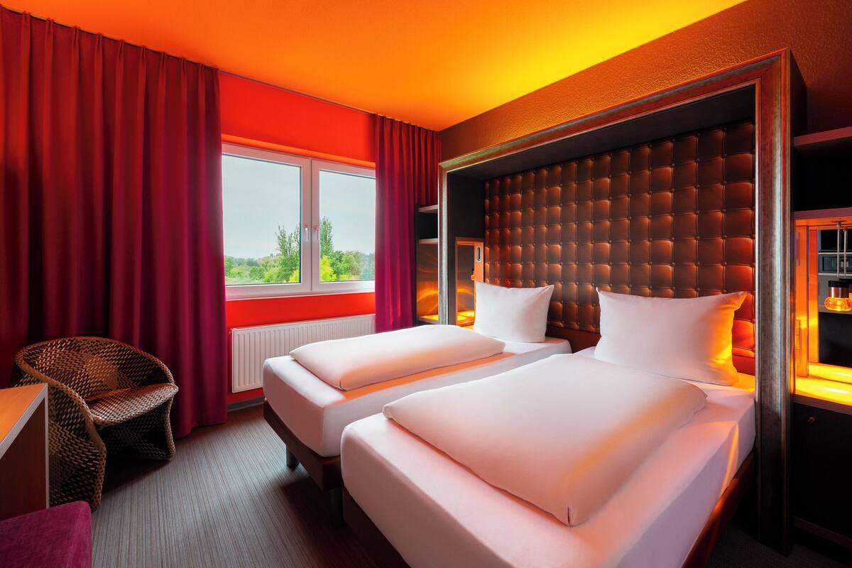 Een hotelkamer met twee bedden, een groot raam en uitzicht op groen.