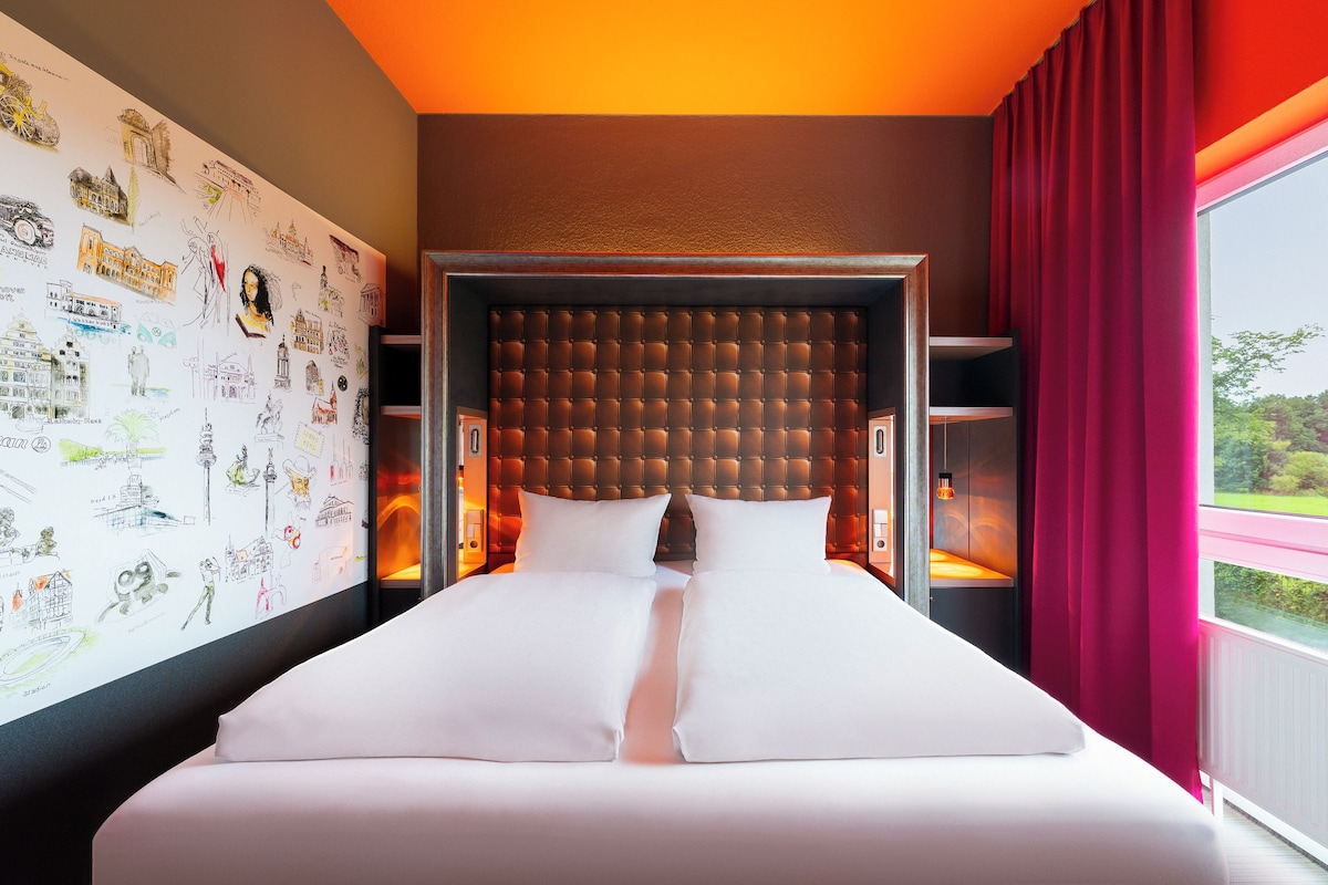 A hotel room with a large bed, a headboard with a tufted design, and a wall decorated with various sketches.