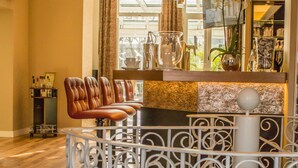 Una zona de bar con barandilla de metal blanco, taburetes de cuero y un columnilla decorativo blanco.