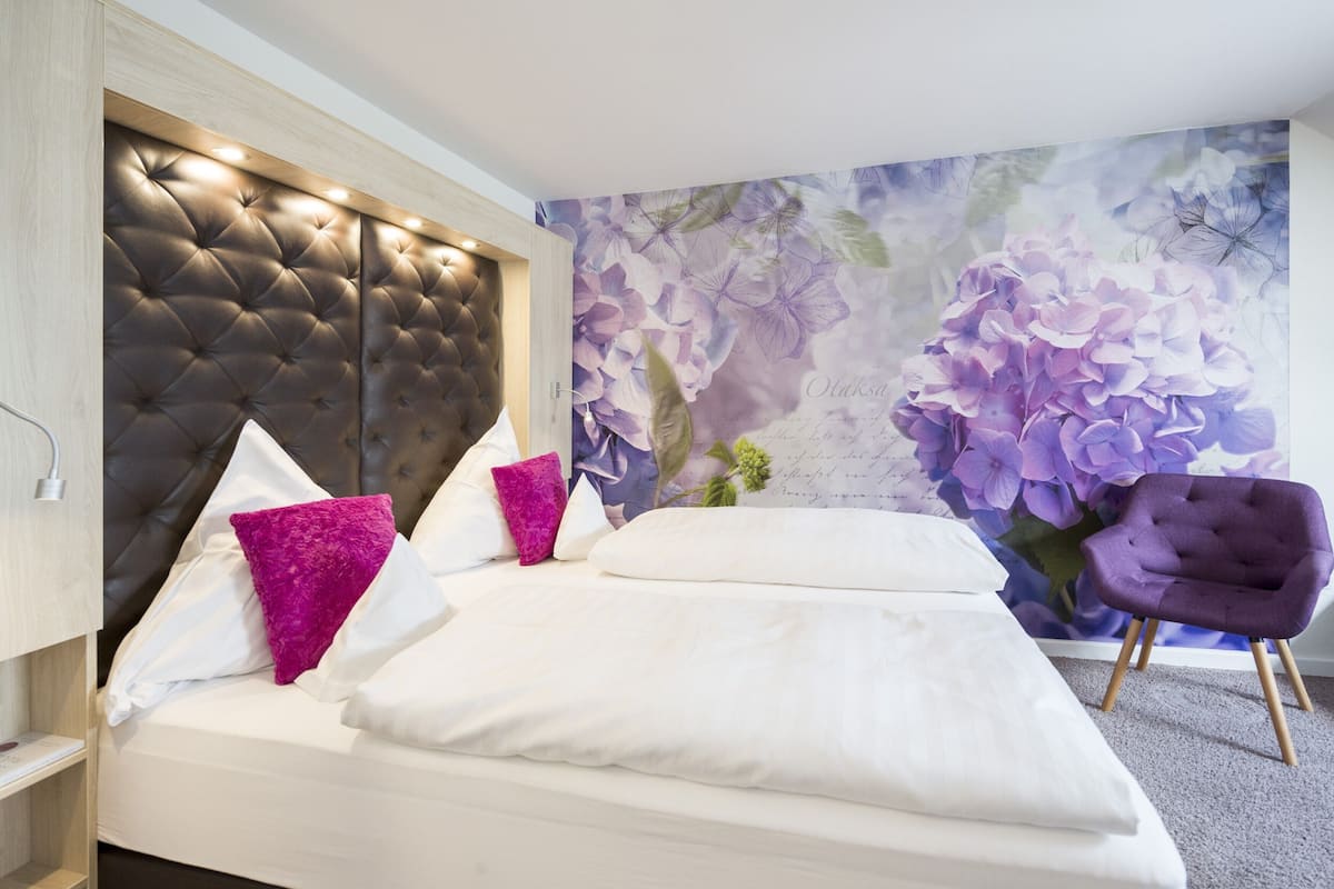 A bedroom with a tufted headboard, white bedding, and a purple chair.