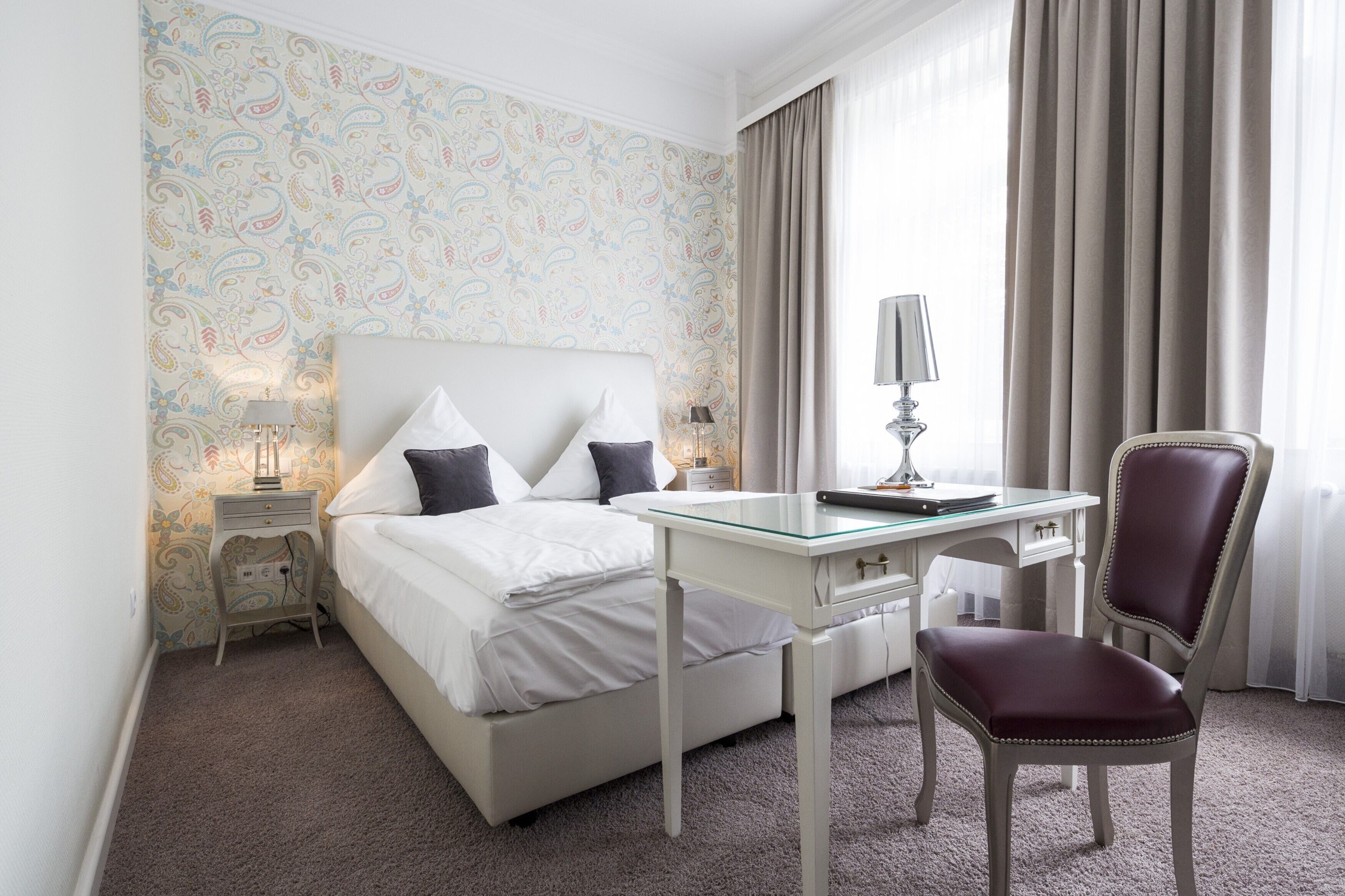 Een hotelkamer met een bed, een bureau, een stoel, een lamp en een nachtkastje.