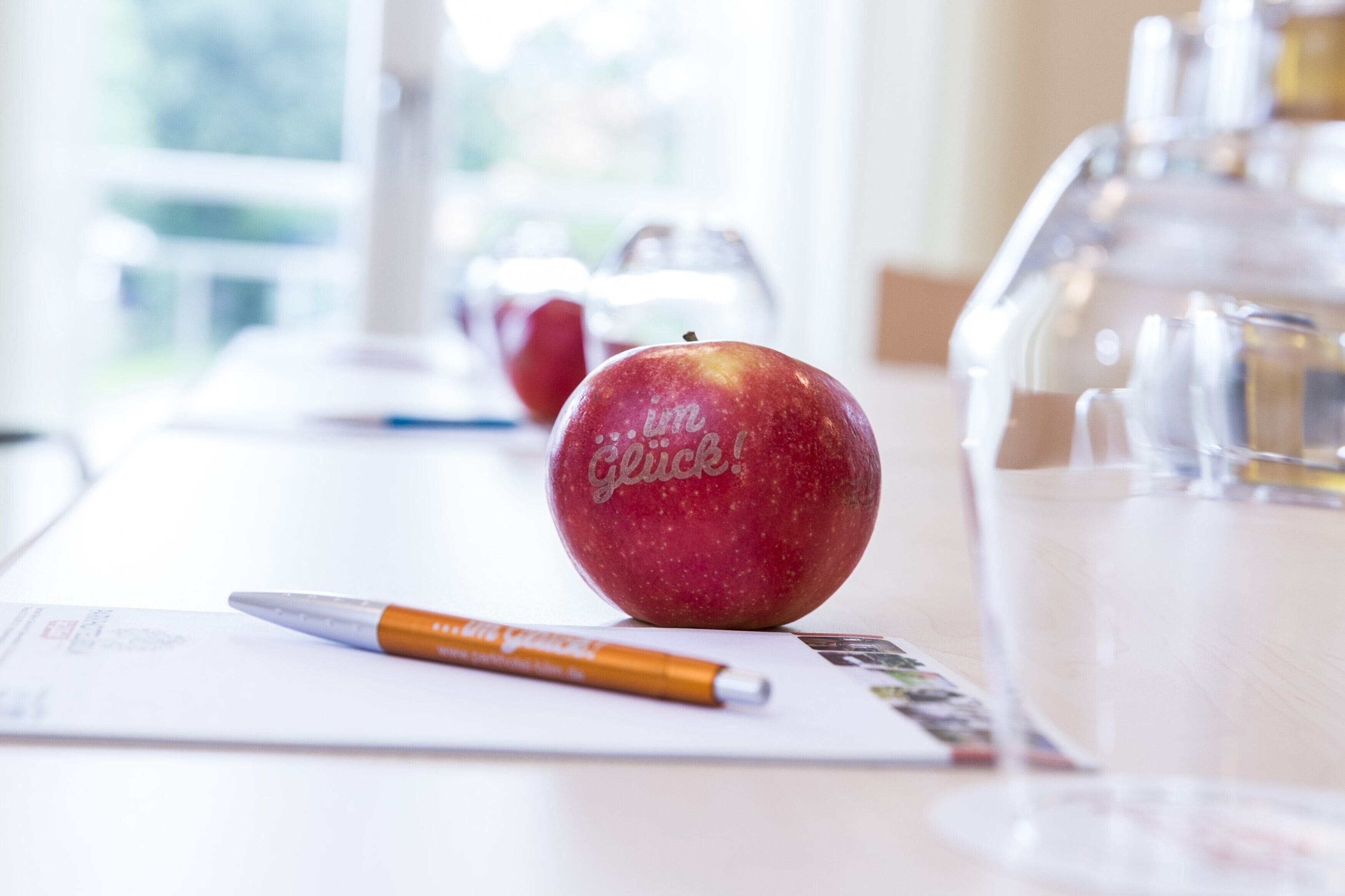Una mesa con una manzana roja, un bolígrafo y una jarrón de vidrio.