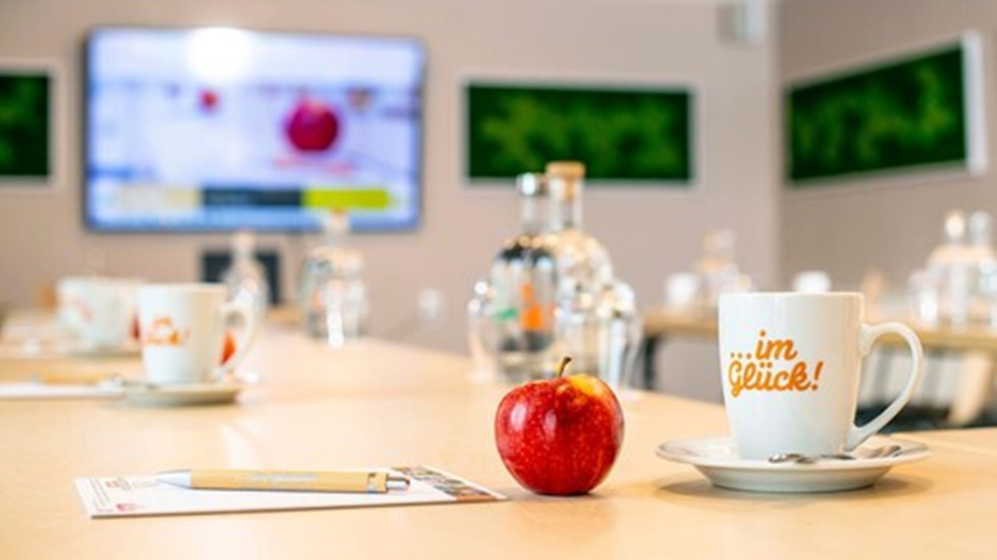 Ett konferensbord med en vit mugg, ett rött äpple och en vattenflaska.