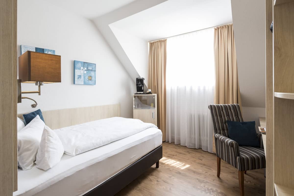 A hotel room with a bed, a chair, a nightstand, a lamp, and a window with curtains.