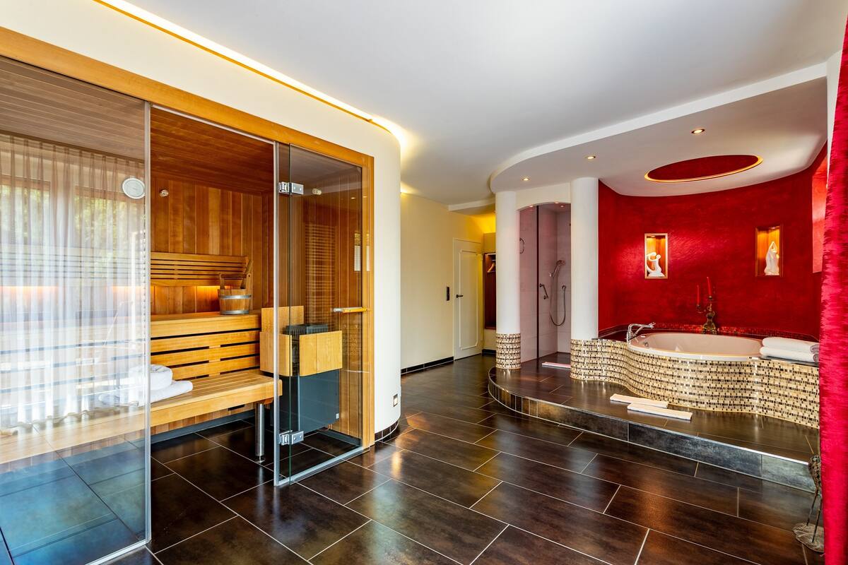 Ein modernes Spa mit Sauna, Dampfbad und einem großzügigen Whirlpool mit roten Fliesen.