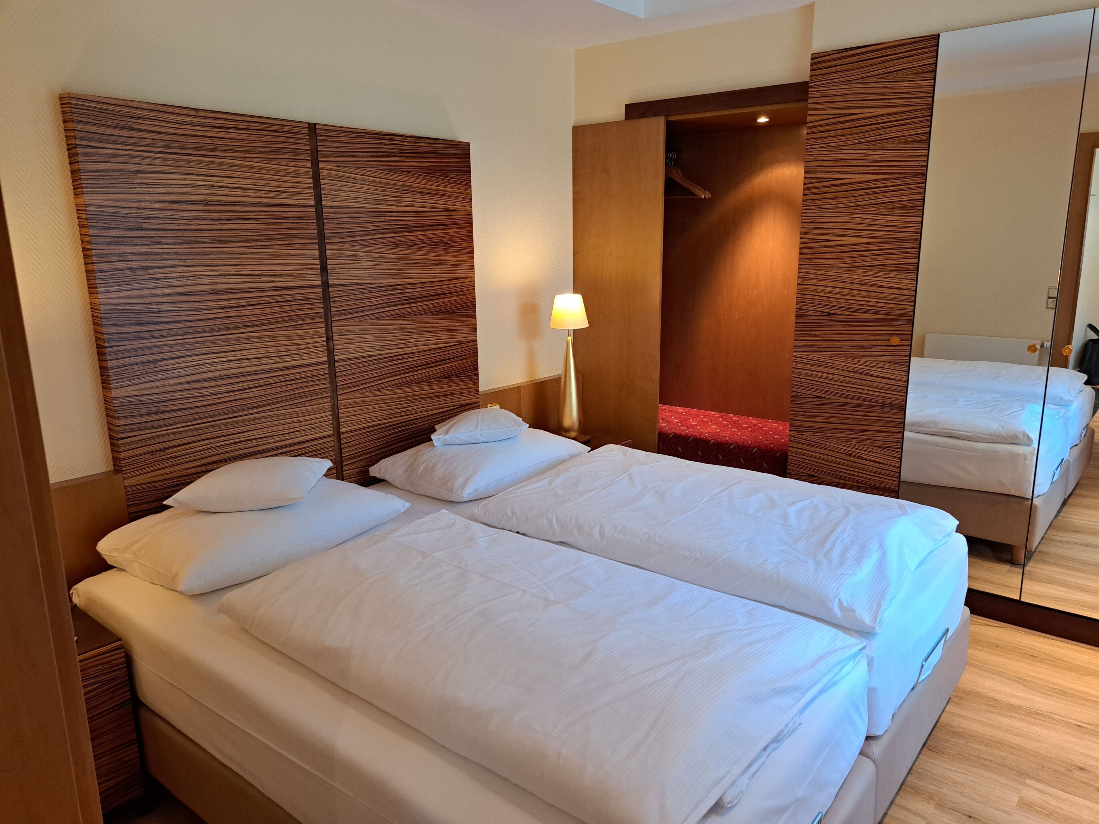 A hotel room with two beds, wooden headboards, a mirror, and a red accent wall.