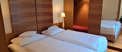 A hotel room with two beds, wooden headboards, a mirror, and a red accent wall.