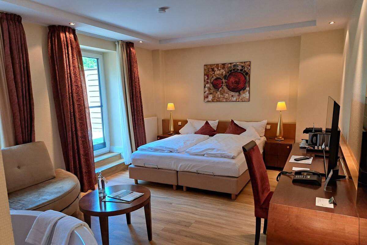 Ein Hotelzimmer mit einem Bett, einem Schreibtisch, einem Sessel, einem kleinen Tisch, einer Couch und einem Fenster mit Vorhängen.