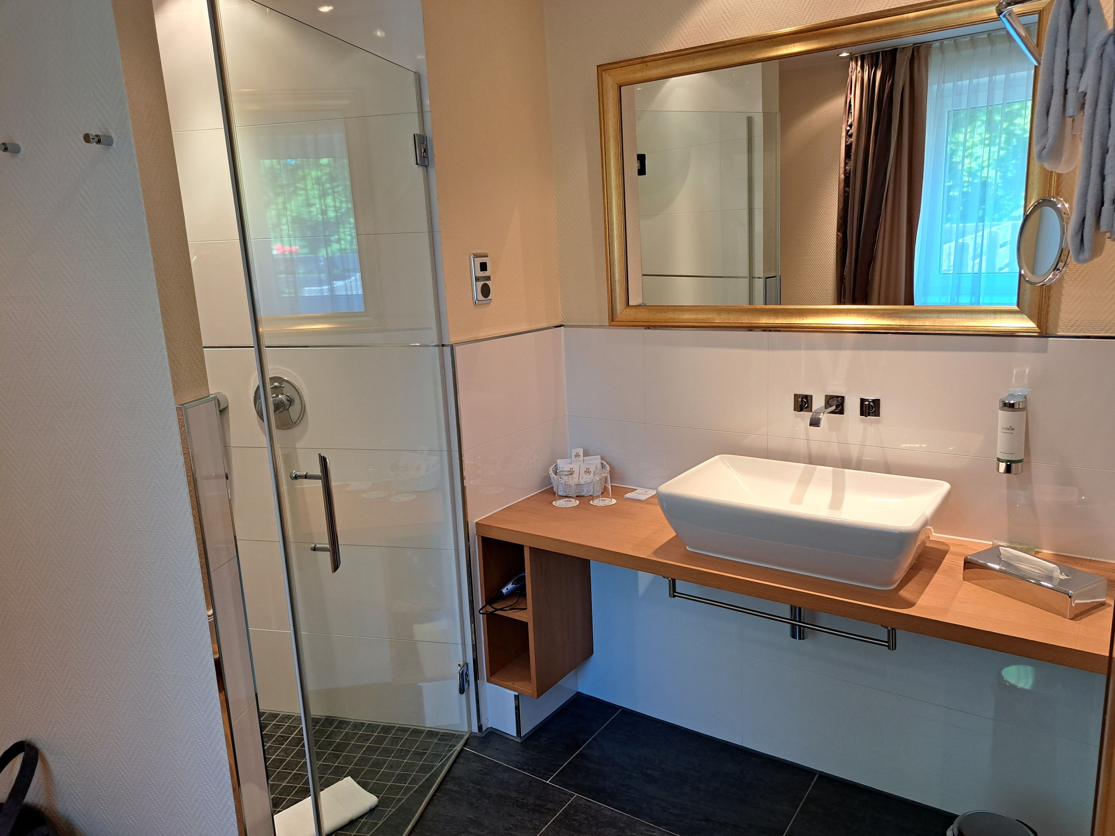 Ein modernes Badezimmer mit Glasdusche, einem Holzkosmetikschrank, einem großen Spiegel und einem Waschbecken.