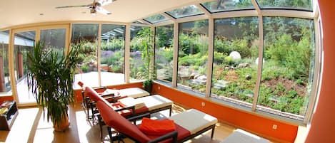 Una habitación luminosa con ventanas amplias, un ventilador de techo y una planta en maceta.