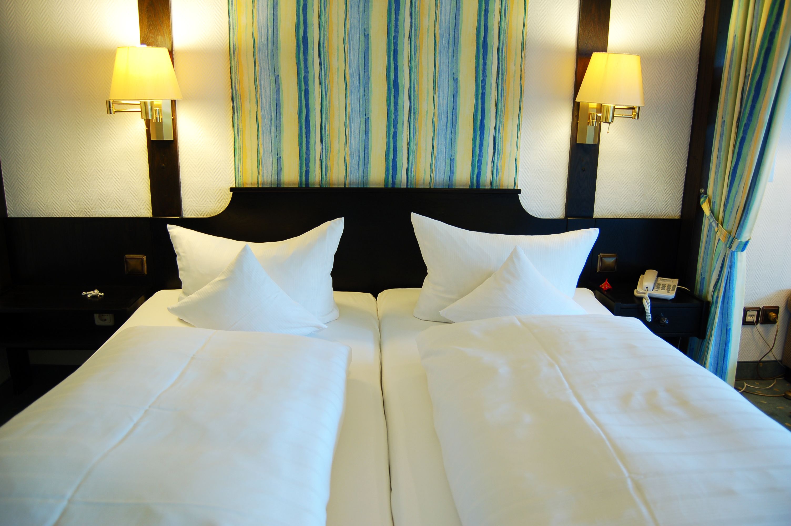 Ein Hotelzimmer mit zwei Betten, einer gestreiften Wand und zwei Nachttischlampen.