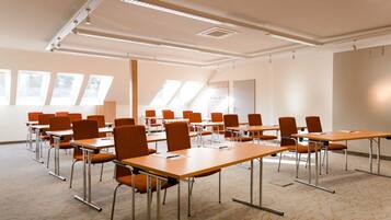 Ein Konferenzraum mit mehreren Tischen und Stühlen, großen Fenstern und einer hohen Decke mit Dachfenstern.
