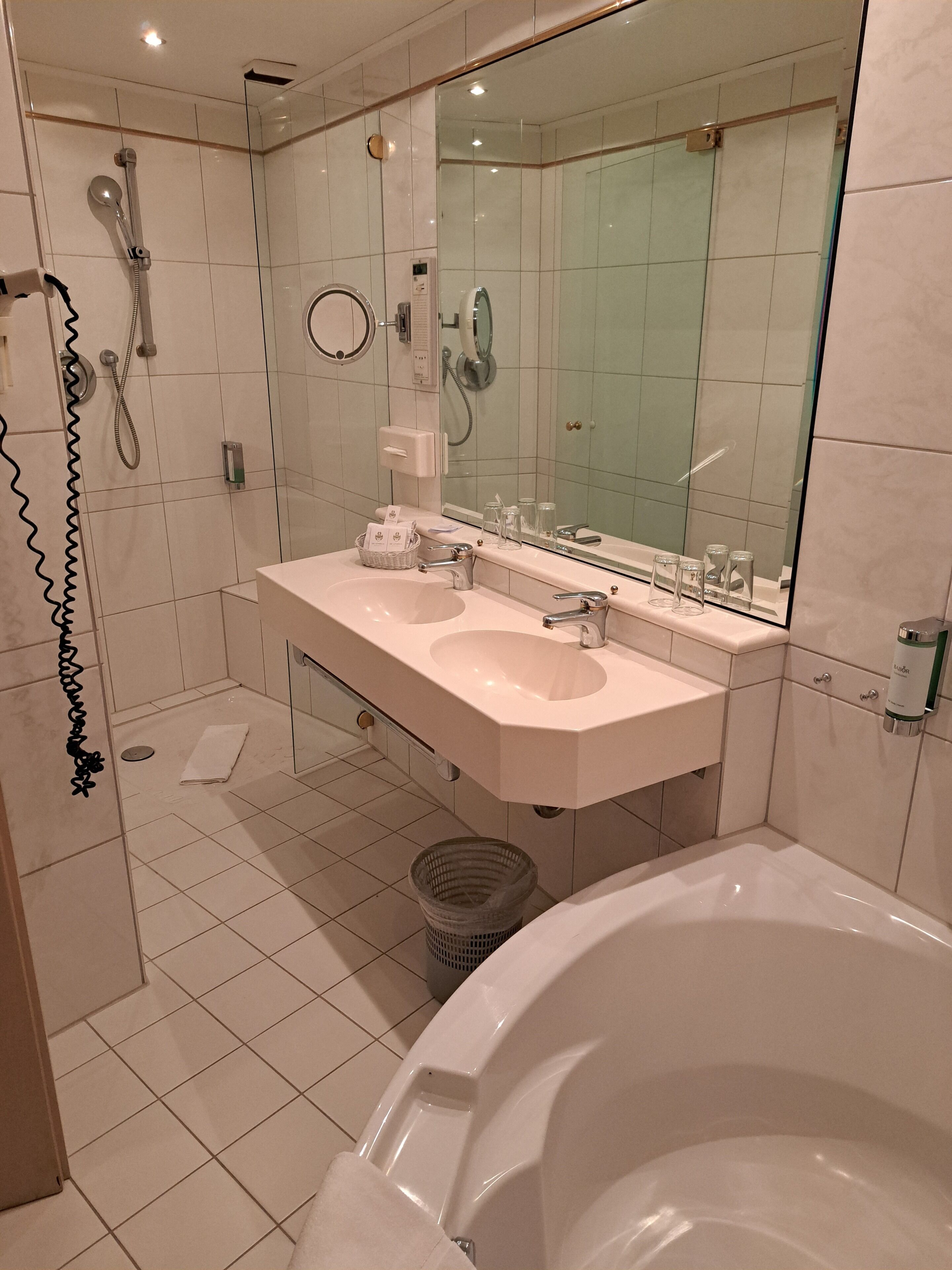 A modern bathroom with a large bathtub, two sinks, a glass shower enclosure, and a mirror above the sinks.