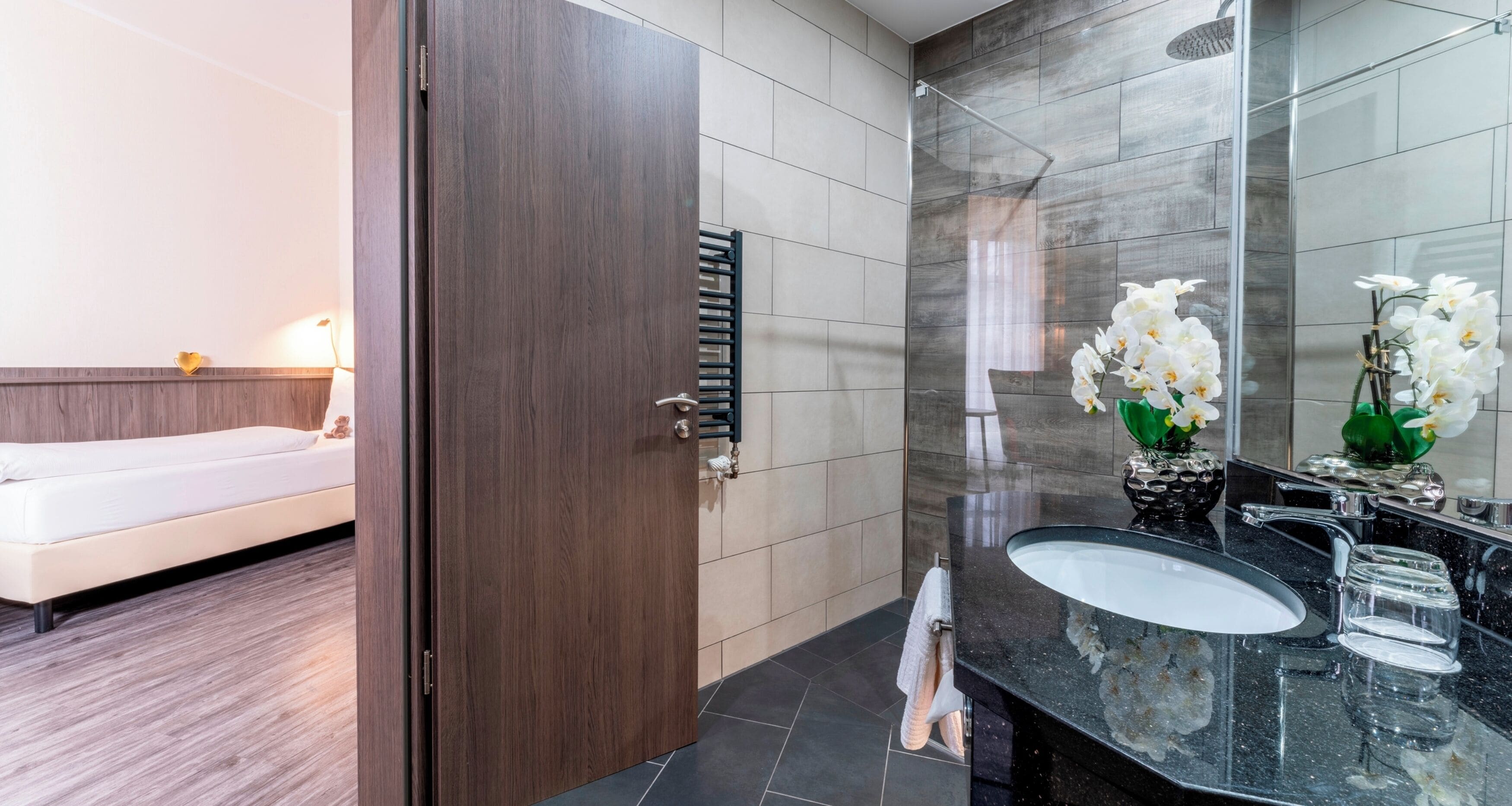 Un baño moderno con una puerta de madera oscura, un lavamanos blanco y una cabina de ducha de vidrio.