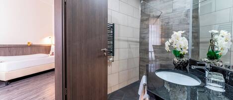 Un baño moderno con una puerta de madera oscura, un lavamanos blanco y una cabina de ducha de vidrio.