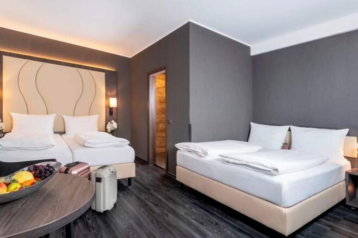 A hotel room with two beds, a round table with fruit, a suitcase, and a wooden floor.