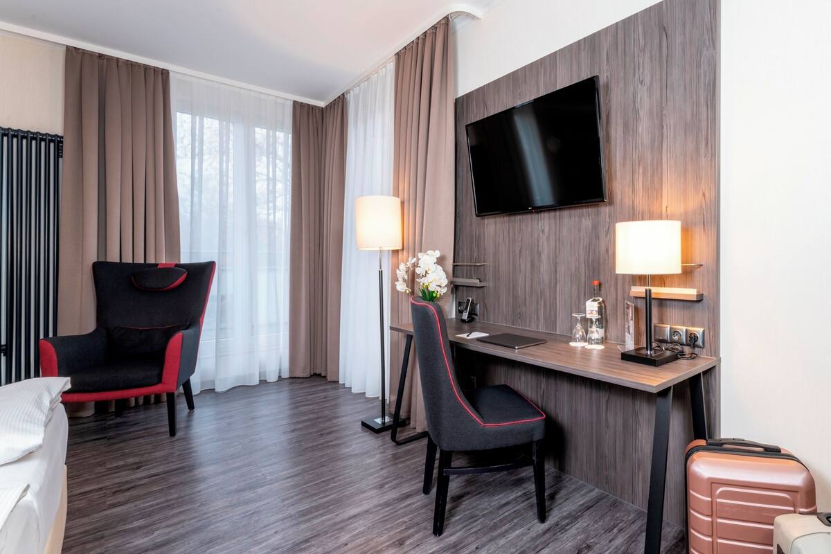 Een hotelkamer met een houten bureau, twee stoelen, een televisie en een bed.