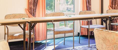 A conference room with a long table and six chairs, large windows with curtains, and a blue carpet.