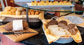 A buffet with various breads and pastries, including croissants and baguettes, displayed on a glass counter.