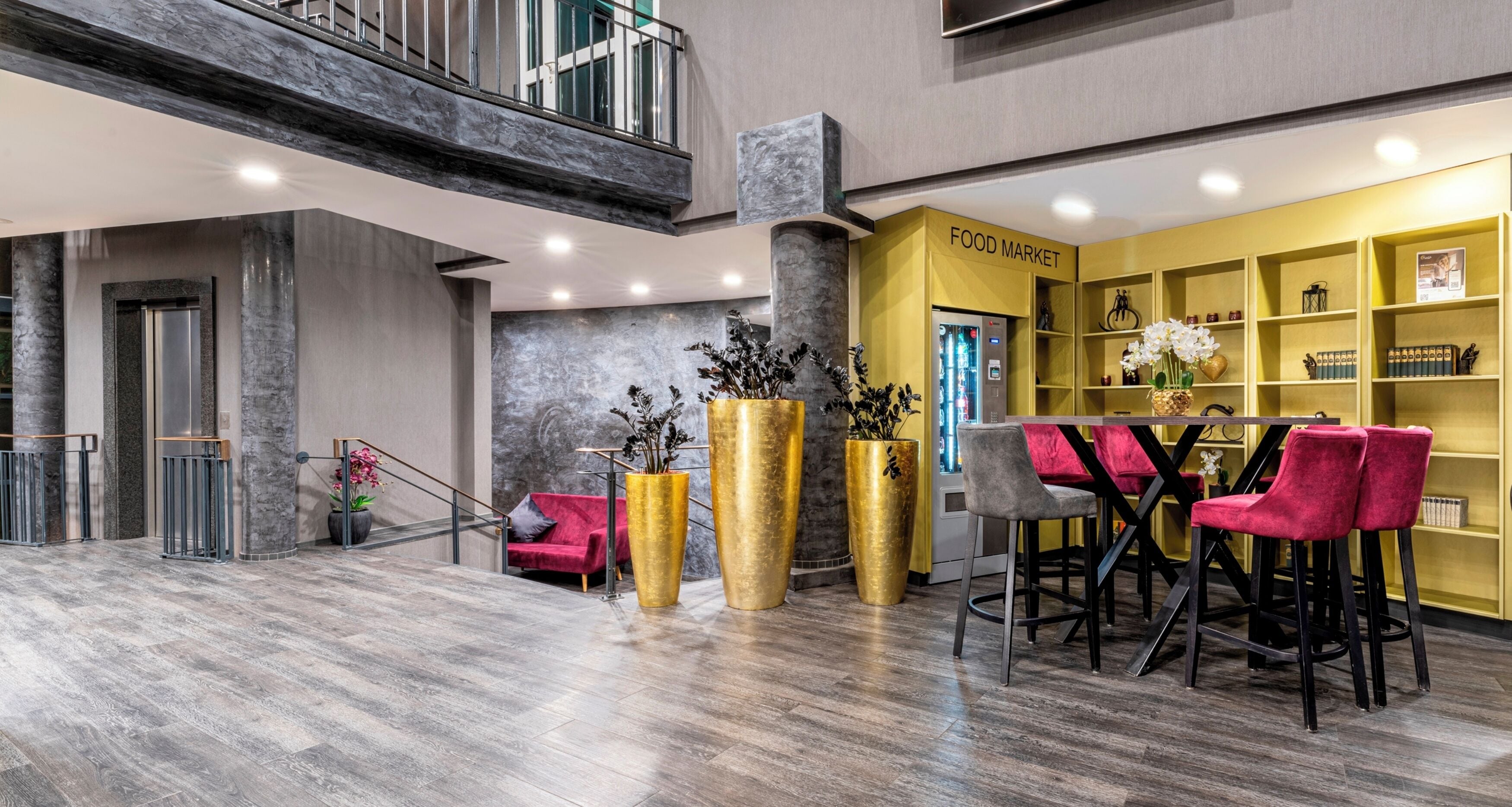 Een moderne lobby met een entresol, een food market gedeelte, en een zithoek met rode stoelen.