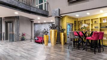 Een moderne lobby met een entresol, een food market gedeelte, en een zithoek met rode stoelen.