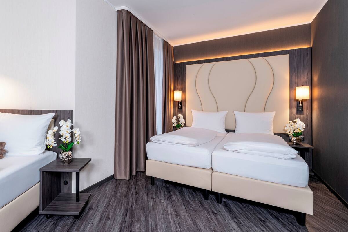 Een hotelkamer met een bed, een eenpersoonsbed, een nachtkastje met een lamp en een vaas met bloemen.