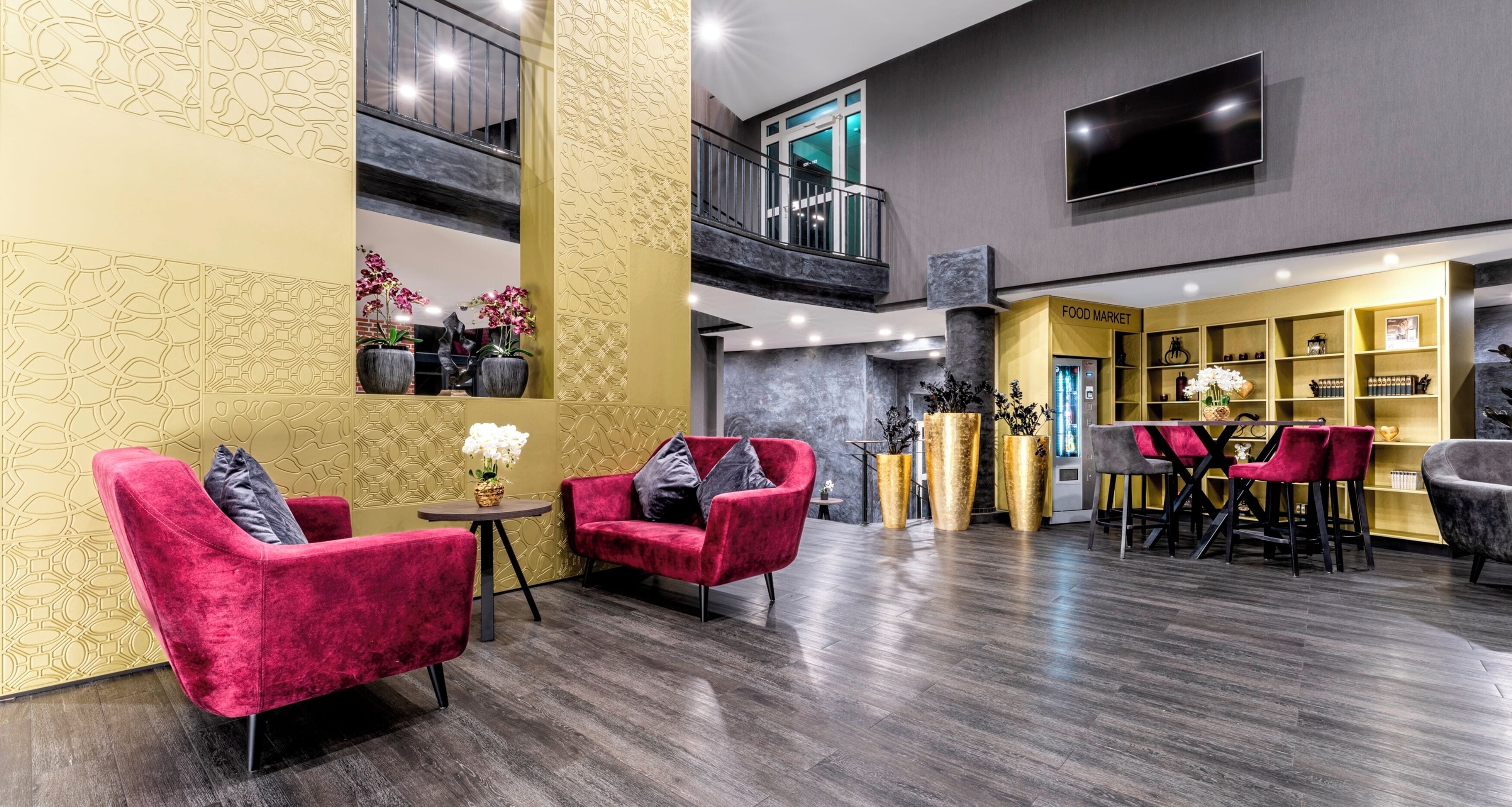 A modern lobby with red chairs, a food market, and a TV on the wall.