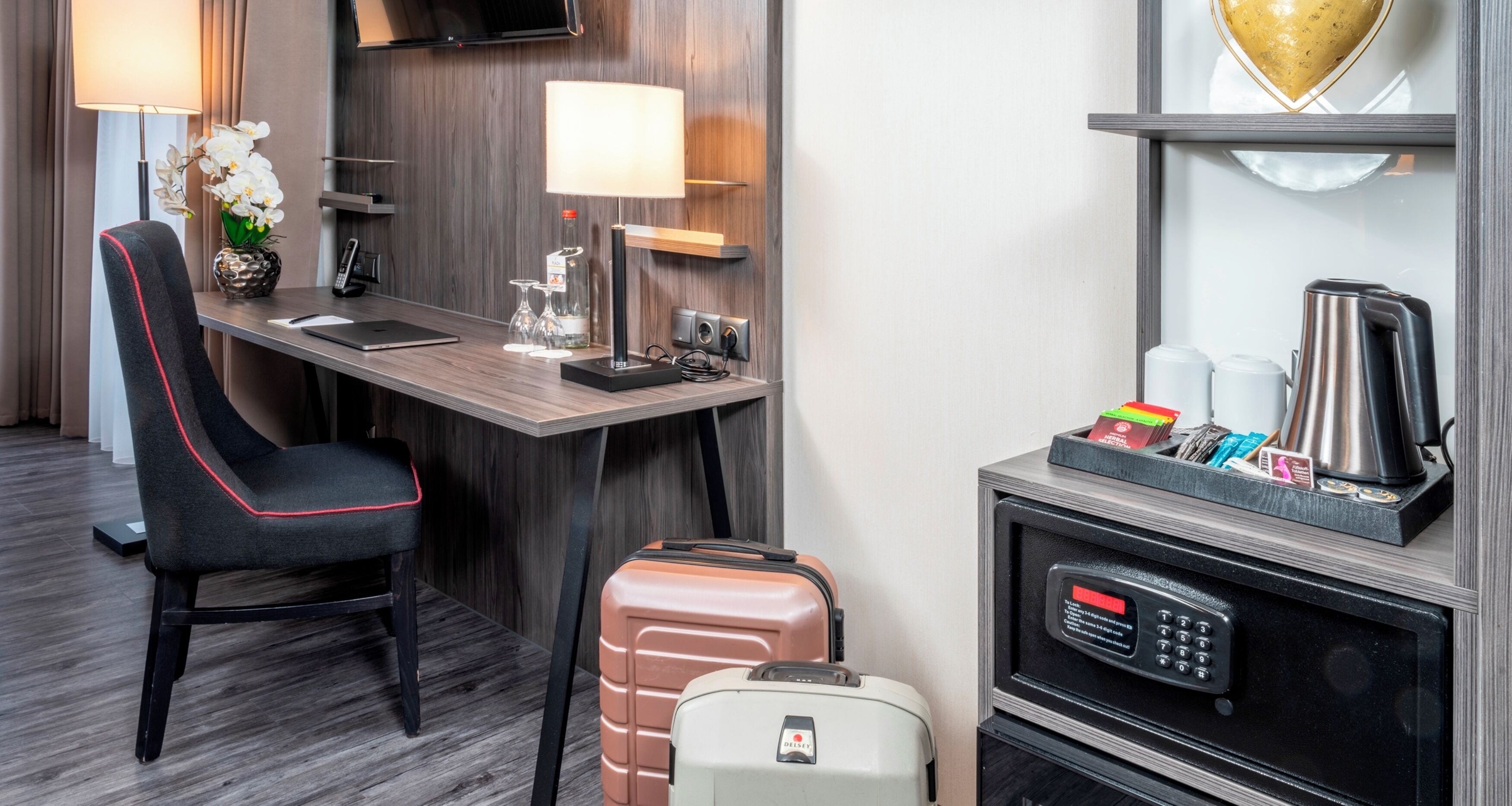 Ein Hotelzimmer mit Schreibtisch, Stuhl, Minibar, Mikrowelle und einem Koffer.