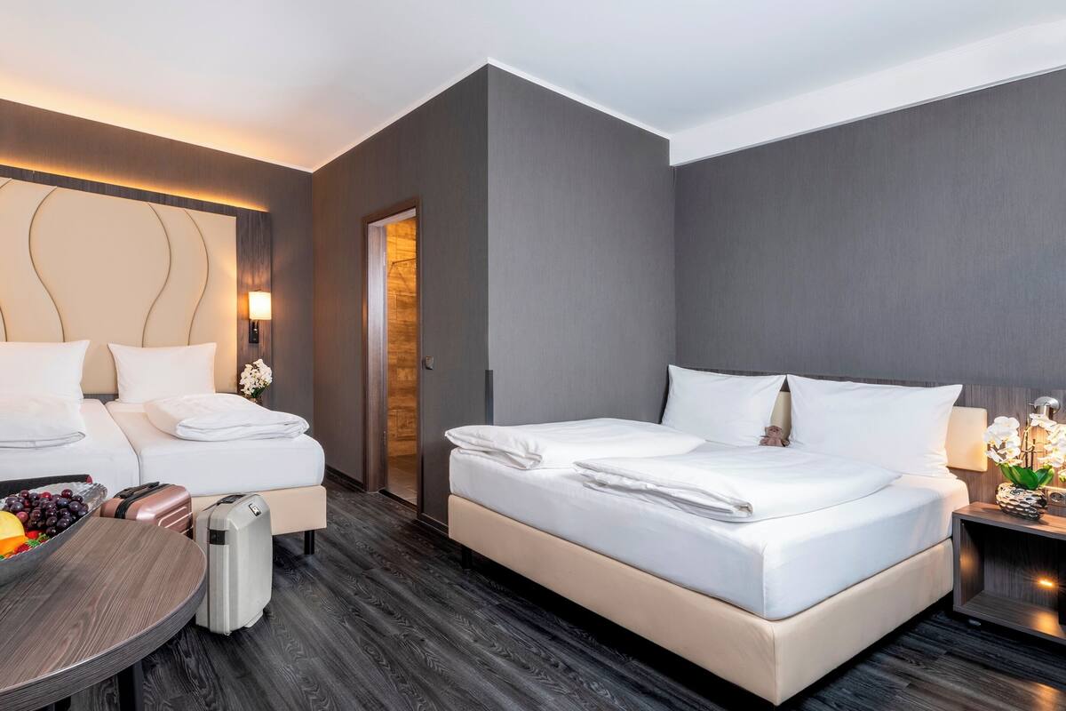 Een moderne hotelkamer met twee bedden, een klein tafeltje met fruit en een koffer.