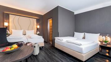 Ein modernes Hotelzimmer mit zwei Betten, einem kleinen Tisch mit Früchten und einem Koffer.