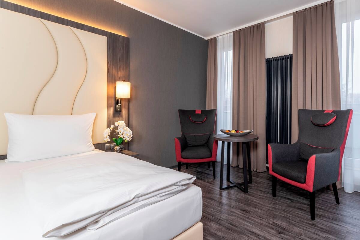 Een hotelkamer met een bed, twee fauteuils, een kleine tafel met een schaal en een raam met gordijnen.