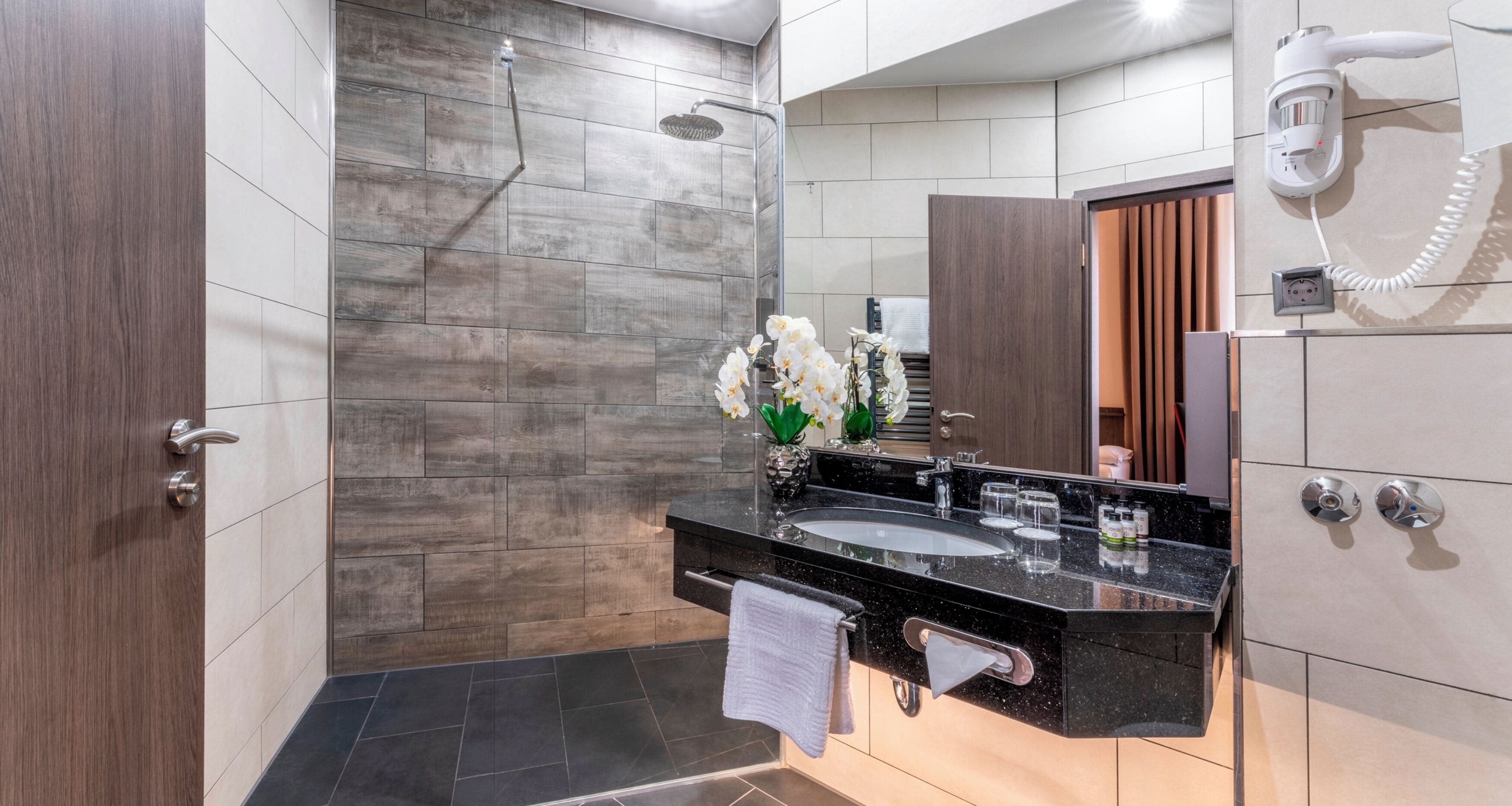Une salle de bain moderne équipée d’une douche, d’un meuble-lavabo avec miroir et d’un sèche-cheveux fixé au mur.