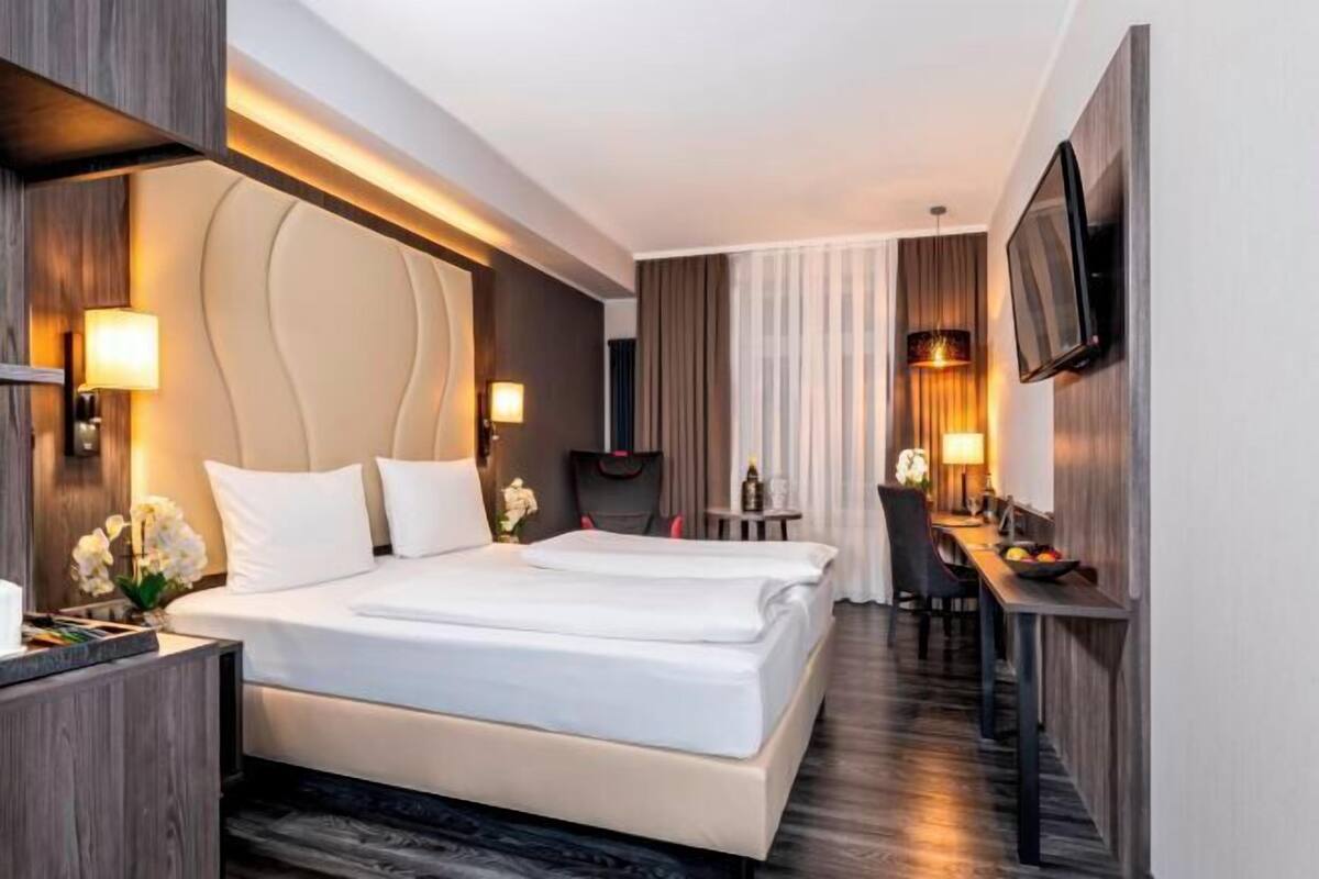 Een hotelkamer met een groot bed, een bureau, een stoel, een televisie en een bijzettafeltje met een lamp.
