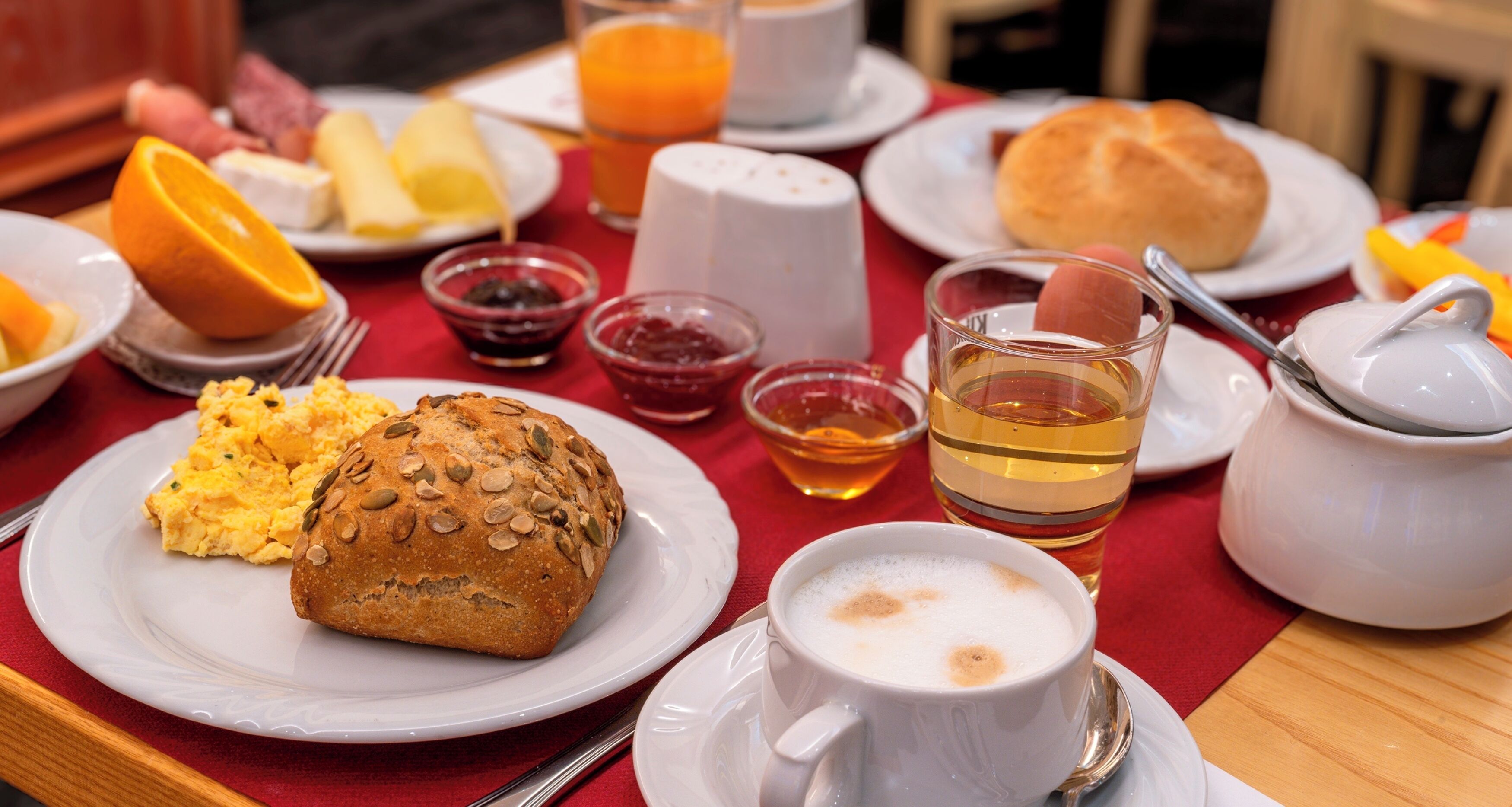 Desayuno con huevos revueltos, un muffin, rodajas de naranja y una taza de café sobre un mantel rojo.