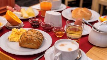 Desayuno con huevos revueltos, un muffin, rodajas de naranja y una taza de café sobre un mantel rojo.