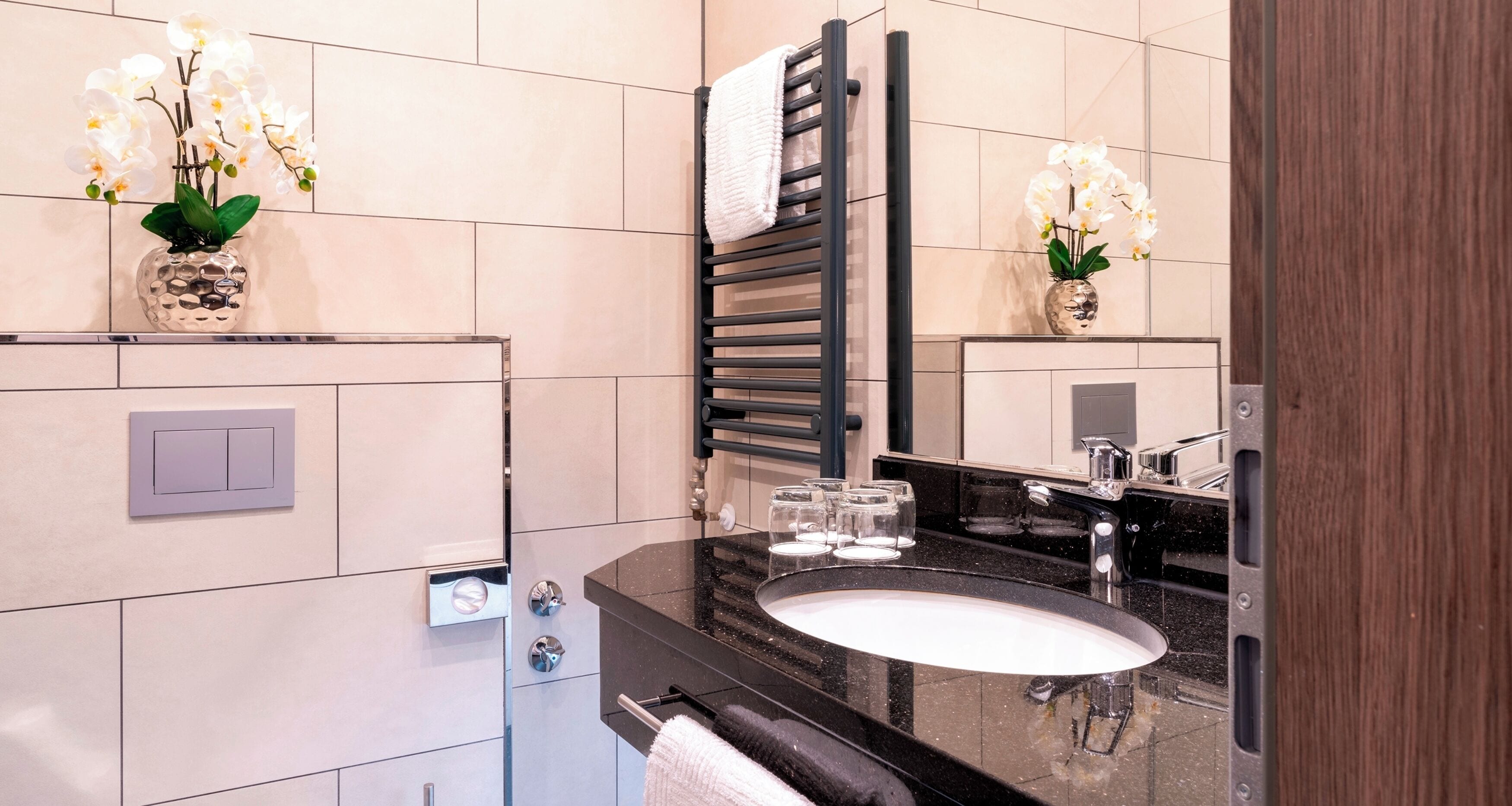 Un baño moderno con lavamanos de encimera negro, un perchero y dos jarrones de orquídeas.