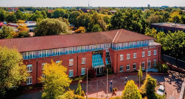 A multi-story brick building with a flat roof, labeled "Park Hotel." It features a prominent glass facade on the ground floor, likely a restaurant or cafe, and multiple windows on the upper floors.