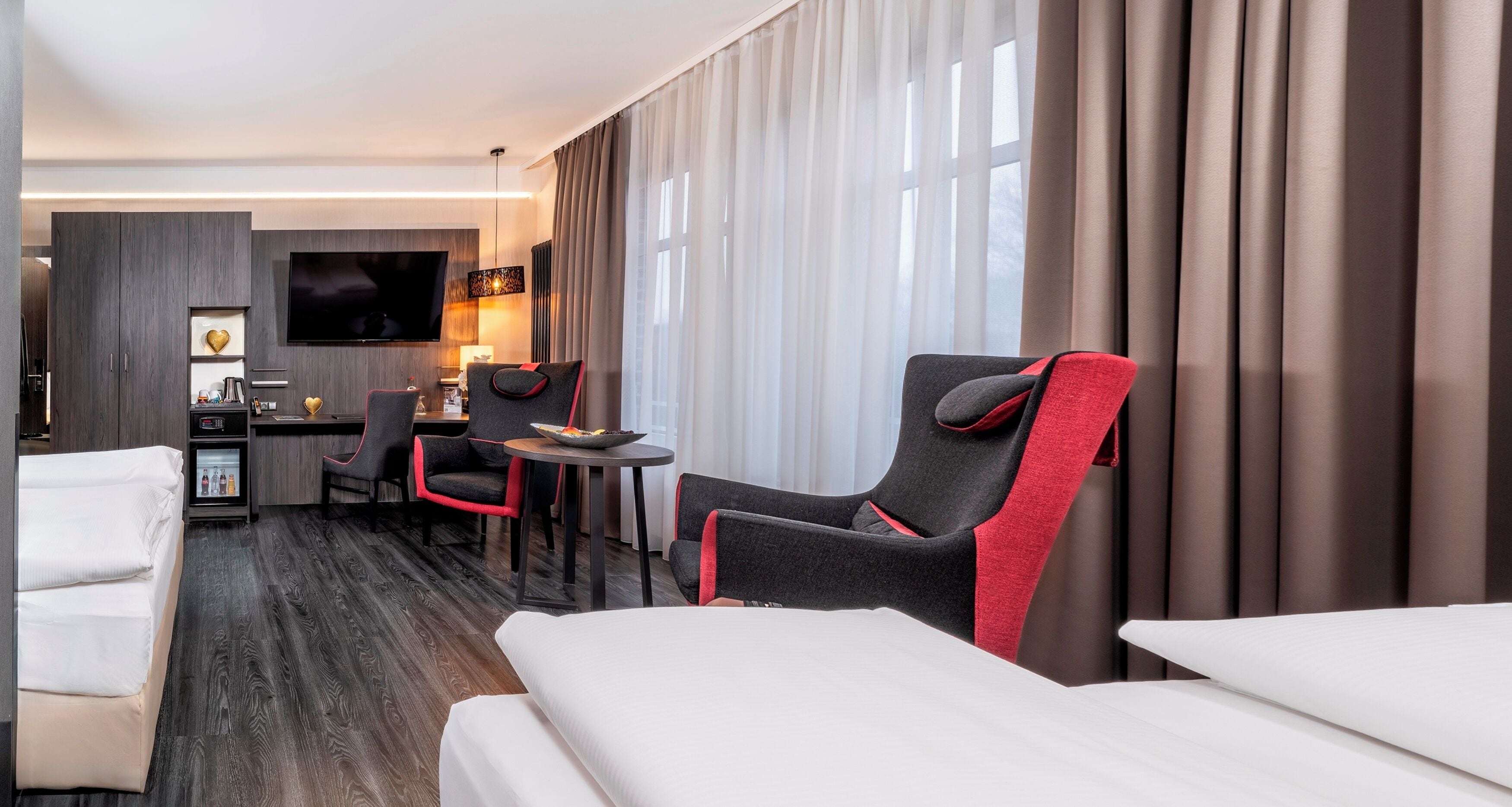 A hotel room with a bed, a desk with a chair, a TV, and a minibar.