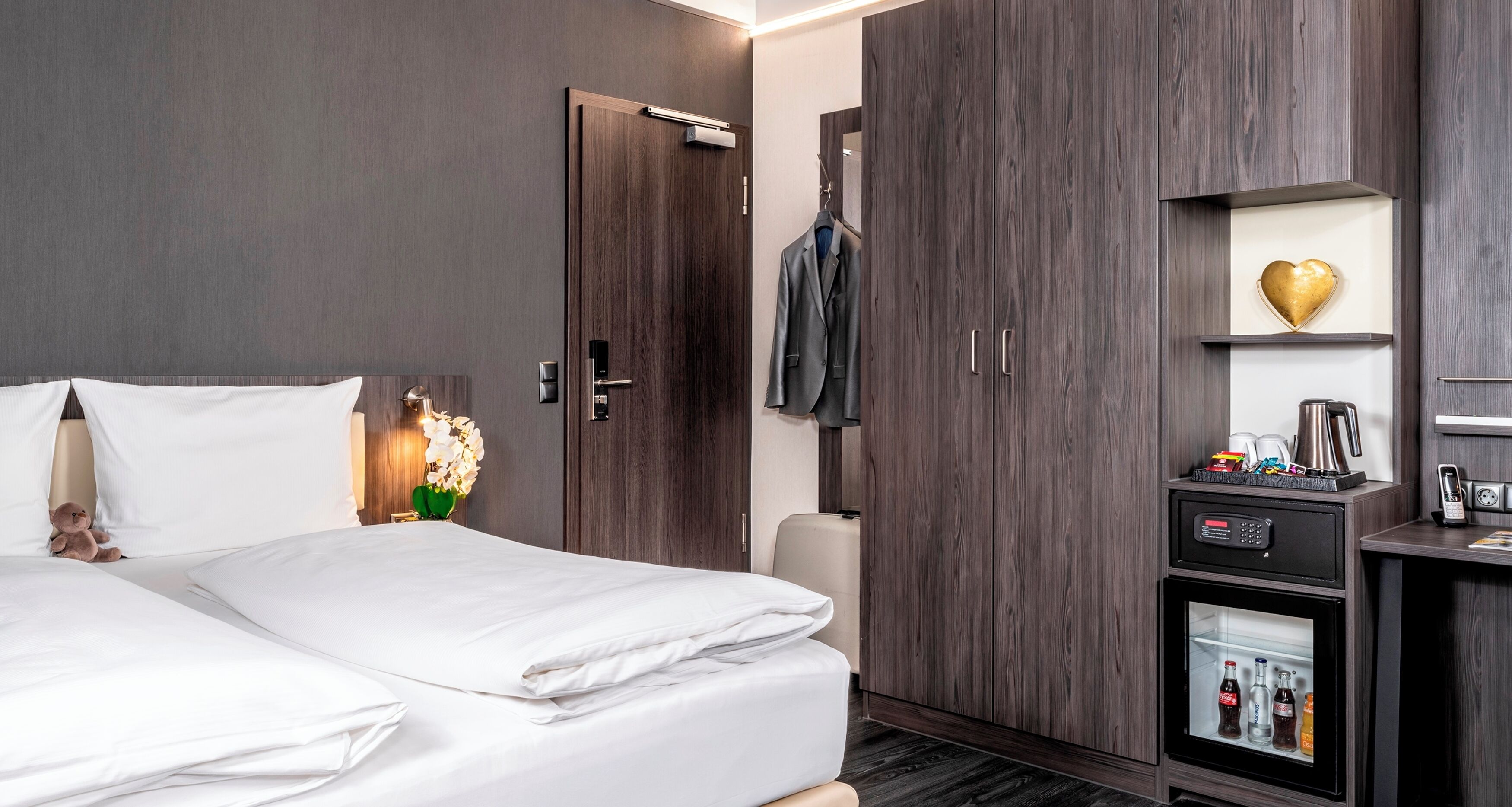 A hotel room with a bed, wardrobe, and minibar.