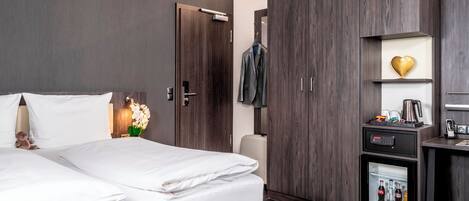 A hotel room with a bed, wardrobe, and minibar.