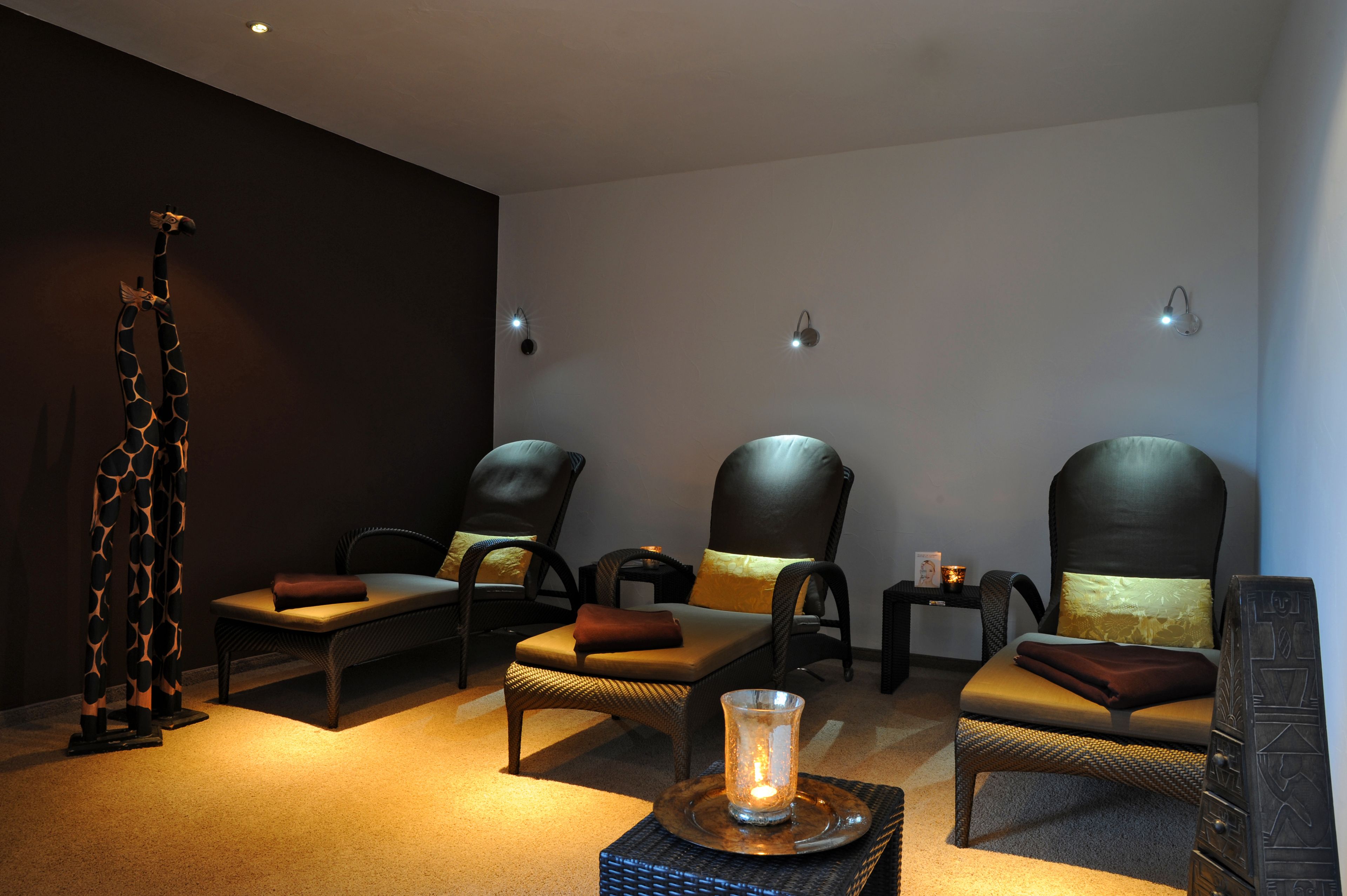 A spa room with three reclining chairs, a massage table, and a decorative giraffe sculpture.