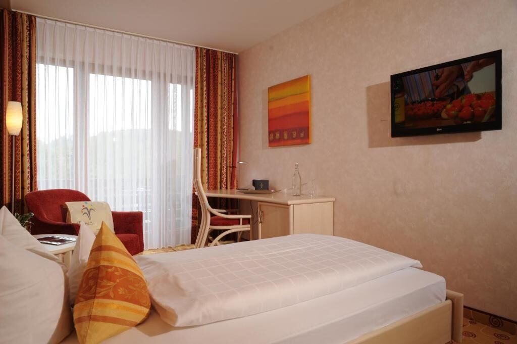 A hotel room with a bed, a desk, a chair, and a television.