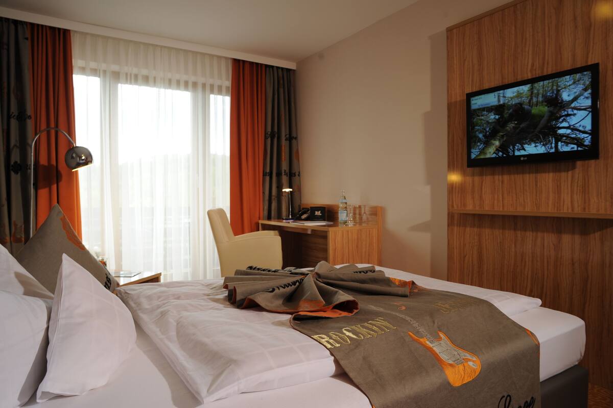 Una habitación de hotel con cama, escritorio, silla, televisión y cortinas.