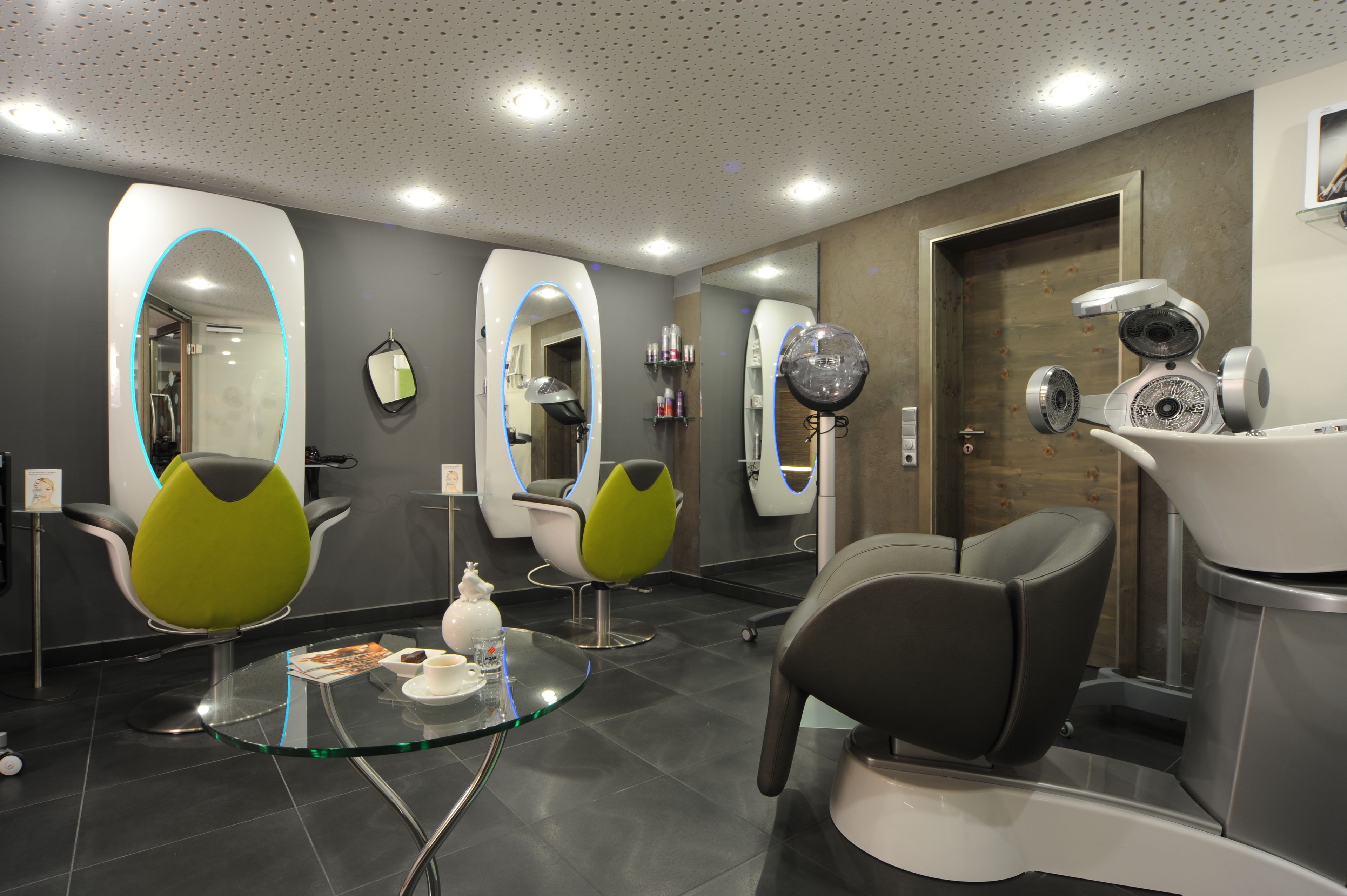 A modern salon with three chairs, a glass table with a cup and saucer, and a door with a hairdryer on it.