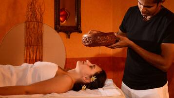 A person receiving a massage in a room with a large mirror, a decorative vase, and a red object on the wall.