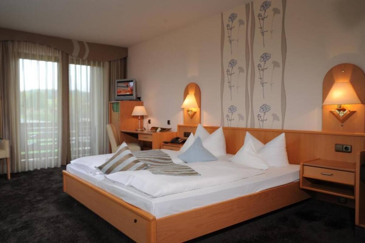 Una habitación de hotel con una cama grande, lámparas de noche, un escritorio y una silla.