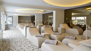 A modern spa room with multiple reclining chairs, a pebble-patterned floor, and a large mirror wall. - Hotel Freund (Voehl)